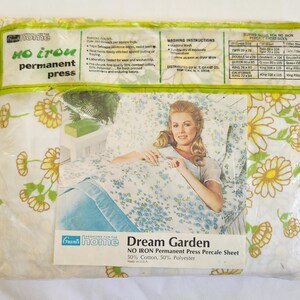 May include: A sealed package of Grants Home Dream Garden no-iron permanent press percale sheets. The packaging features a woman on a bed with floral sheets. The sheets have a white background with yellow and green flowers and blue floral accents.