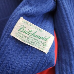 May include: A blue polyester tag with green text that reads "Bulchmaid" and "100% Polyester". The tag also includes care instructions: "Machine Wash-Warm", "Delicate Cycle Tumble Dry", "Low Remove Promptly Cool Iron", and "Ephrata, PA". A white circle with the number "34" is printed on the tag.