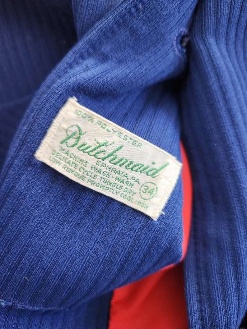 May include: A blue polyester tag with green text that reads "Bulchmaid" and "100% Polyester". The tag also includes care instructions: "Machine Wash-Warm", "Delicate Cycle Tumble Dry", "Low Remove Promptly Cool Iron", and "Ephrata, PA". A white circle with the number "34" is printed on the tag.