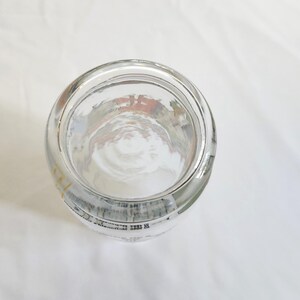 May include: A clear glass jar with a wide mouth and a rounded bottom. The jar has a white label with black text.