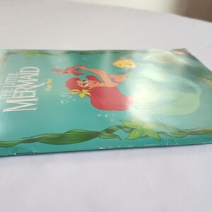 Puede incluir: Un paquete plano y rectangular de Disney The Little Mermaid Play Set con un fondo verde azulado e ilustraciones de algas verdes. El frente muestra una sirena de cabello rojo, un peque&ntilde;o pez amarillo y el texto The Little Mermaid Play Set.
