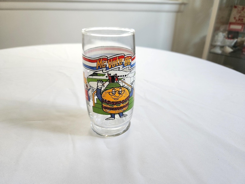 May include: A clear glass with a colorful illustration of a hamburger character with the text "McVote '86".