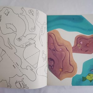 Puede incluir: Un libro de actividades abierto que muestra contornos en blanco y negro de personajes de Disney, incluidos el Rey Trit&oacute;n, &Uacute;rsula y Flounder en la p&aacute;gina izquierda, con formas recortables de colores de terreno submarino y peces a la derecha.