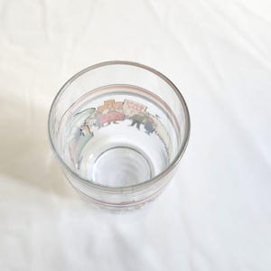 May include: A clear glass drinking glass with a colorful cartoon illustration of people marching around the rim.