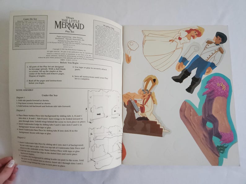 Puede incluir: Un libro de juego de Disney La Sirenita con instrucciones impresas y personajes recortables que incluyen una novia, un novio y una figura religiosa. Las p&aacute;ginas contienen texto, diagramas e ilustraciones coloridas de los personajes.