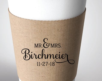 May include: A white to-go coffee cup with a black lid and a brown paper sleeve. The sleeve has the text "MR. & MRS. Birchmeier 11.27.18" printed on it.