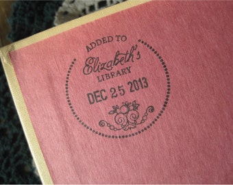 May include: A close-up of a pink book cover with the text "ADDED TO Elizabeth's LIBRARY DEC 25 2013" in a circular design. The book's edge is a light tan color.