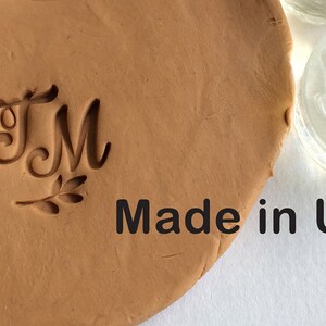 May include: A close-up of a clay imprint of the letters "TM" with a small leaf design below. The text "Made in USA" is visible below the imprint.