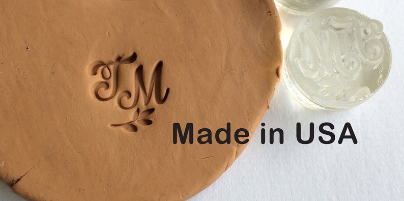 May include: A close-up of a clay imprint of the letters "TM" with a small leaf design below. The text "Made in USA" is visible below the imprint.