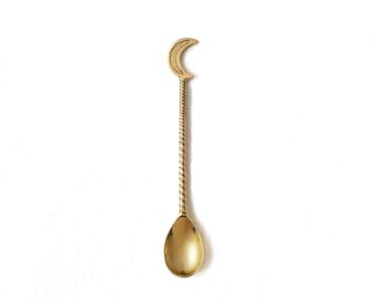 May include: A gold-colored spoon with a crescent moon design at the top. The handle has a twisted rope design, and the spoon's bowl is teardrop-shaped. The spoon is set against a white background.