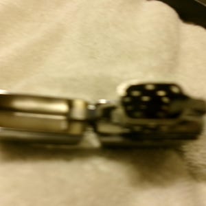 May include: A silver-toned metal lighter, open to reveal the interior. The lighter's top section is black with white polka dots. The lighter is on a light-colored, textured surface.