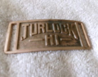 Könnte beinhalten: Eine Gürtelschnalle aus Messing mit den eingeprägten Worten "TURLOCK HI".