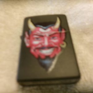 May include: Black lighter with a red devil face graphic. The devil has yellow horns and a goatee.