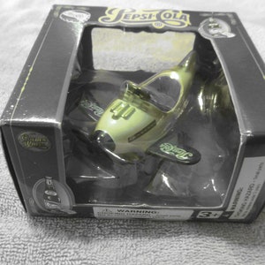 May include: A black box with a clear plastic window showing a yellow toy airplane with "Pepsi Cola" printed on the wings. The box has a "Golden Wings" logo and a "3+" age recommendation.