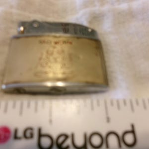 Puede incluir: Encendedor vintage con tapa plateada y cuerpo dorado. El cuerpo tiene las palabras "OLD WORK" y una imagen. El encendedor est&aacute; sobre una superficie blanca.