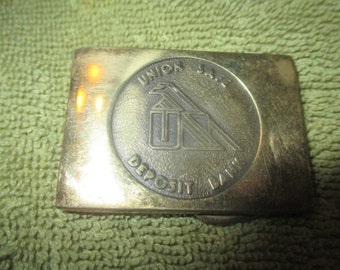May include: A brass belt buckle with a circular design featuring the words "Union Safe Deposit Bank" and a stylized building with a bird on top.