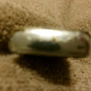 May include: A silver-colored, rectangular metal object with rounded edges. The object has a reflective surface with some discoloration. The item is resting on a textured, tan surface.