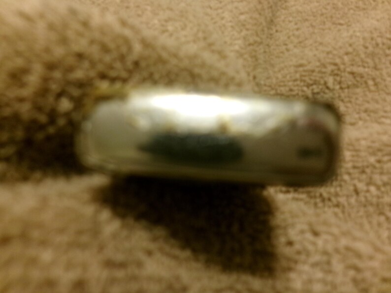 May include: A silver-colored, rectangular metal object with rounded edges. The object has a reflective surface with some discoloration. The item is resting on a textured, tan surface.