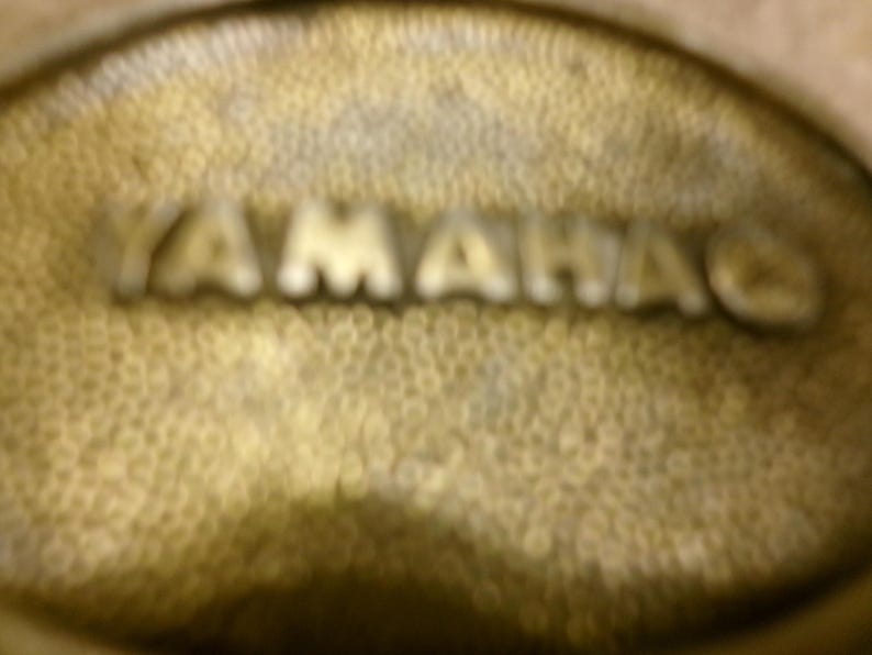 May include: Close-up of a textured, golden-colored surface with the embossed word "YAMAHA" in silver. The surface has a dimpled pattern, and the letters are slightly blurred.