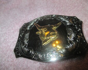 May include: A silver belt buckle with an ornate design featuring a gold bull's head in the centre.