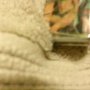 May include: A rectangular metal lighter with a colorful image of a person in a bikini. The lighter has a silver base and a glossy finish. The background is a light tan color.