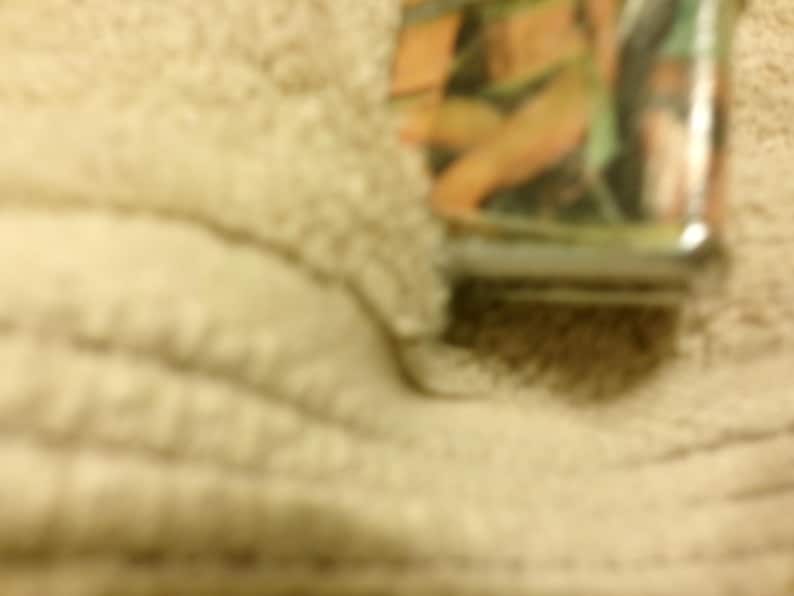 May include: A rectangular metal lighter with a colorful image of a person in a bikini. The lighter has a silver base and a glossy finish. The background is a light tan color.