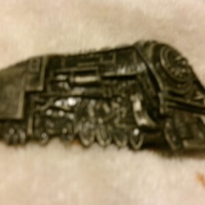 May include: A detailed, dark gray train model with visible wheels, smokestack, and cab. The model is a vintage steam locomotive, showcasing intricate design elements. The train is set against a neutral background.