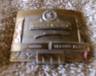 May include: A gold-toned metal belt buckle with the words "National Buckle" and "The Winningest" engraved on it.