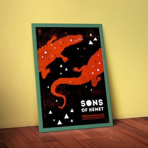 May include: A black and white poster with a red and white illustration of two crocodiles. The poster has the text "Sons of Kemet" and "Green Man Festival 2017" on it.
