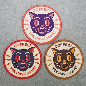 May include: Three round embroidered patches featuring a cartoon cat design. Each patch has a white background with a red, brown, or orange border. The cat has purple or brown fur, large eyes, and an open mouth. The text "COFFEE? YES HAVE SOME!" is printed around the cat.