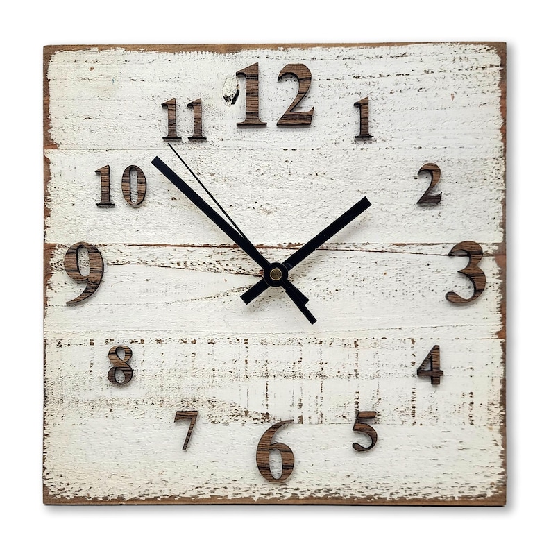 May include: White wooden square clock with black hands and black Roman numeral hour markers. The clock has a distressed white paint finish and a brown wood frame.