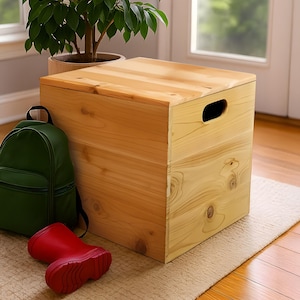 May include: A light-colored wooden storage box with a lid and a handle cut-out. A green backpack and a pair of red rain boots are next to the box. A potted plant is in the background.