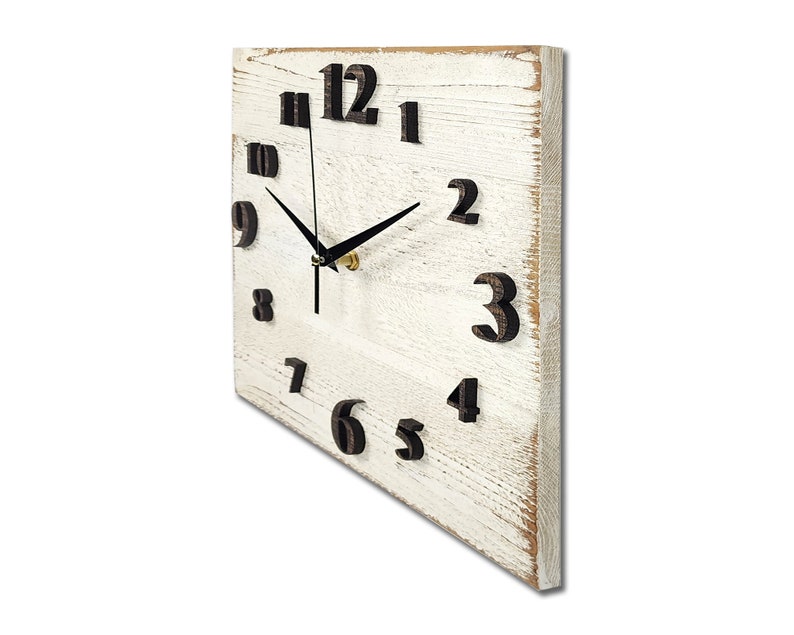 May include: White wooden square clock with black numbers and hands. The clock has a distressed white paint finish and the numbers are raised and slightly angled.