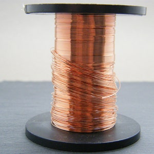 May include: A spool of copper wire wound around a black plastic bobbin. The wire is a shiny, reddish-brown color.