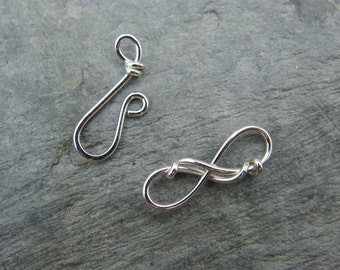 May include: Two silver metal clasps for jewelry making. One clasp is a simple loop, the other is a more intricate infinity symbol design.