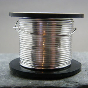 Könnte beinhalten: Eine Spule silberfarbenen Drahtes auf einem schwarzen Kunststoffsockel. Der Draht ist fest gewickelt und hat eine glänzende Oberfläche.