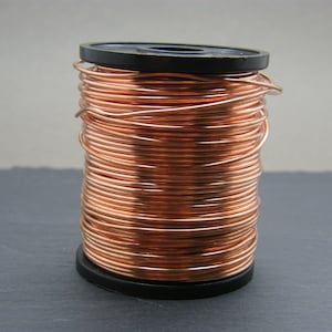 Könnte beinhalten: Eine Spule mit Kupferdraht, die um einen schwarzen Kunststoffspulenkörper gewickelt ist. Der Draht ist glänzend und hat eine rotbraune Farbe.