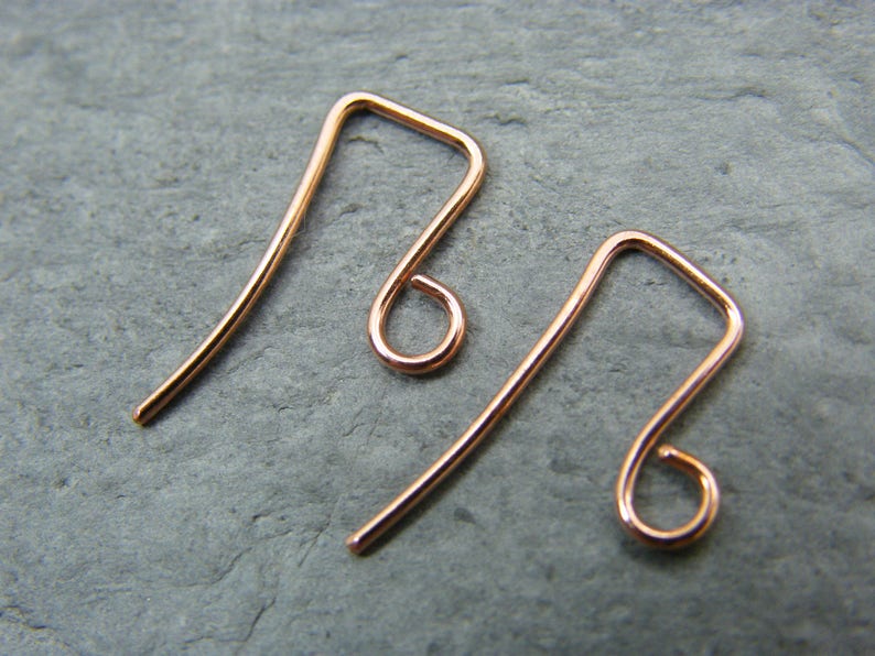 May include: Two rose gold earring hooks. The hooks are made of wire and have a simple, elegant design.