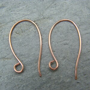 May include: A pair of rose gold ear wires, also known as French hooks, are shown against a gray background. The ear wires are made of a thin, delicate wire and have a simple, elegant design.