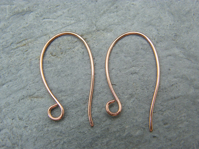 May include: A pair of rose gold ear wires, also known as French hooks, are shown against a gray background. The ear wires are made of a thin, delicate wire and have a simple, elegant design.