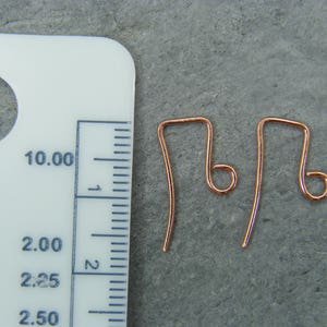 May include: Two copper earring hooks, each measuring approximately 2.25 inches in length, are shown next to a ruler. The hooks are made of a thin, flexible wire and have a small loop at the top.