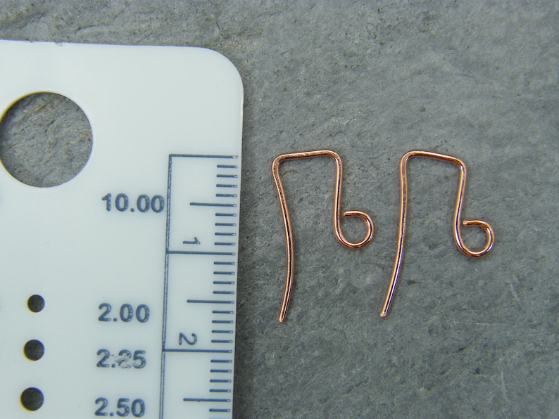 May include: Two copper earring hooks, each measuring approximately 2.25 inches in length, are shown next to a ruler. The hooks are made of a thin, flexible wire and have a small loop at the top.