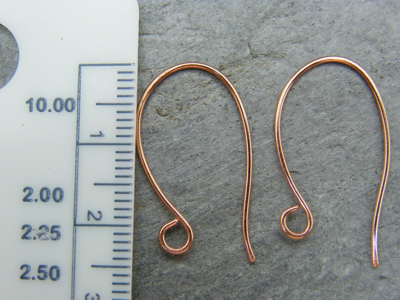 May include: Two copper earring hooks, each measuring approximately 2.5 inches in length. The hooks are made of a thin, flexible wire and have a small loop at the end.