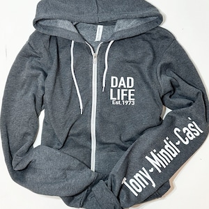 May include: A gray zippered hoodie with the text "DAD LIFE Est. 1973" on the front and "Tony-Mindl-Casi" on the left sleeve.