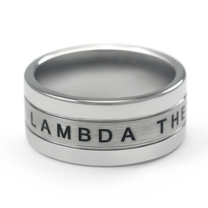 May include: A silver ring with a brushed finish and the word "LAMBDA" engraved on the band.