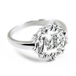 Könnte beinhalten: Ein silberner Ring mit einem sternförmigen Design und einem kleinen Diamanten in der Mitte. Der Ring zeigt den Buchstaben "A" in der Mitte des Sternendesigns.