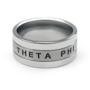 Puede incluir: Un anillo de plata con acabado cepillado y una inscripci&oacute;n en negro que dice "THETA PHI".