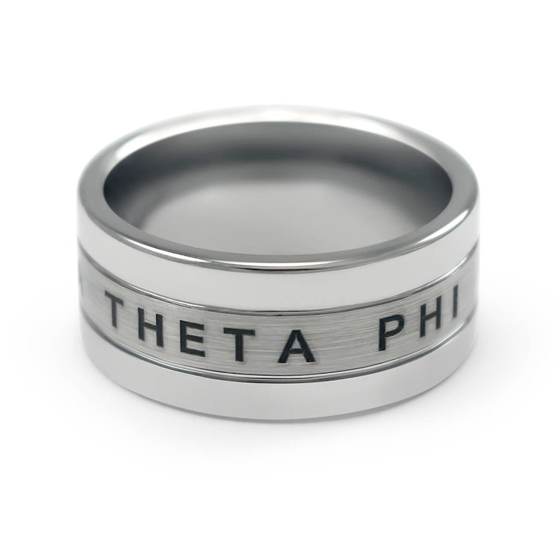 Puede incluir: Un anillo de plata con acabado cepillado y una inscripci&oacute;n en negro que dice "THETA PHI".
