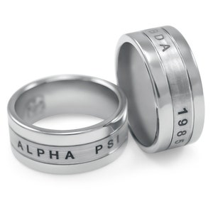 Op de afbeelding: Twee zilveren ringen met gegraveerde tekst. De ene ring zegt "ALPHA PSI" en de andere zegt "BDA 1985".