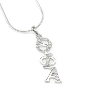 Könnte beinhalten: Silberkette mit einem Anhänger mit den griechischen Buchstaben 'ΦΙΔΑ', die mit kleinen Diamanten besetzt sind, und einem Kreis mit Diamanten am Rand.